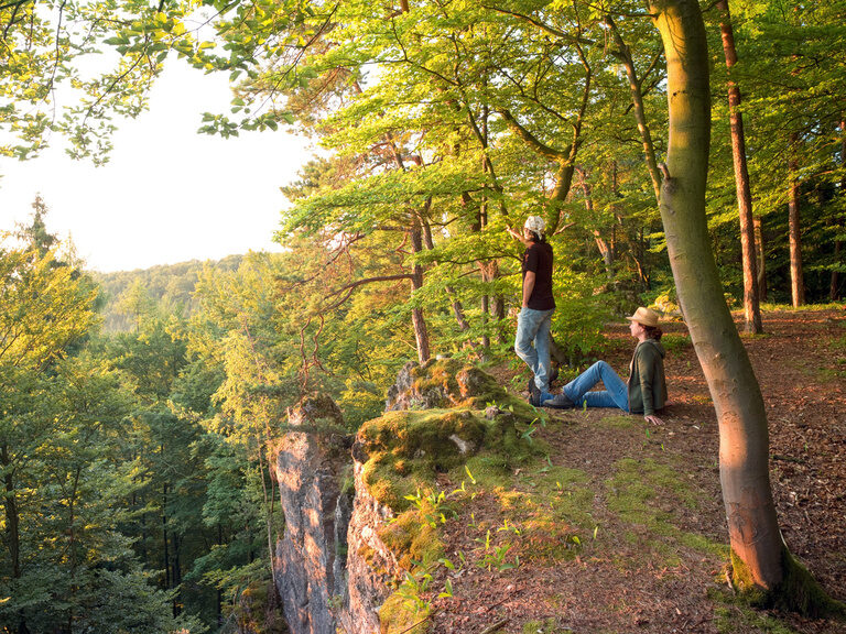 Zwei Personen sitzen am Rand eines Abhangs und schauen über den Oberpfälzer Wald
