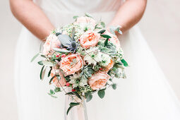 Eine Braut hält einen Strauß aus rosa und grünen Blumen in der Hand.