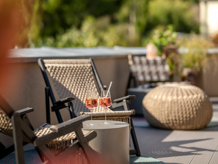 Zwei Cocktails stehen auf einem Beistelltisch neben zwei Liegen auf der sonnigen Terrasse