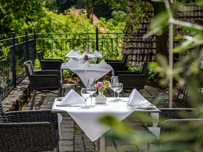 Gedeckte Tische stehen auf dem Pflaster der Terrasse und Pflanzen in Töpfen bieten die perfekte Atmosphäre.
