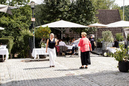 Eine Gruppe von Menschen sitzt draußen an Tischen unter schattigen Sonnenschirmen.