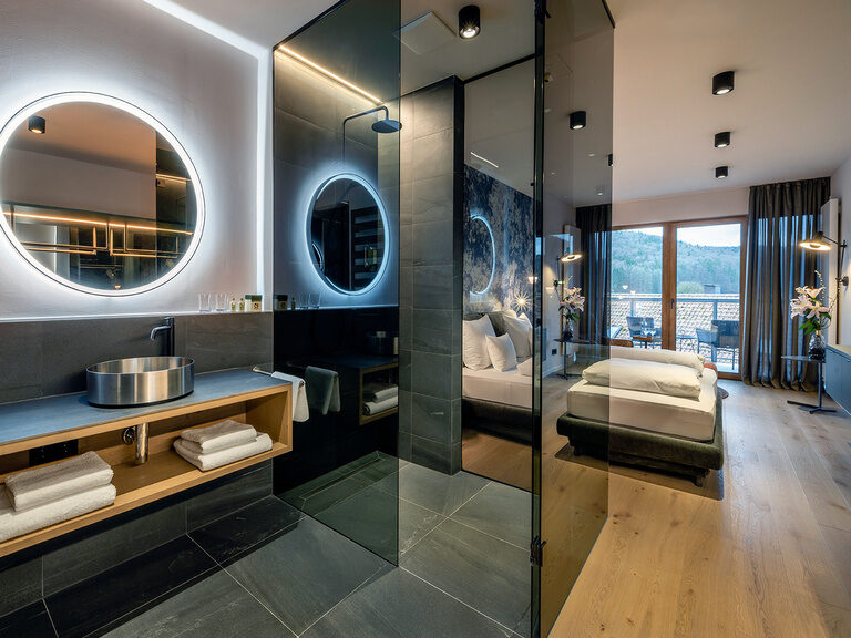 Das elegante, offene Badezimmer im Premium-Zimmer des Wellnesshotels bietet einen modernen Stil mit einer großen Regendusche