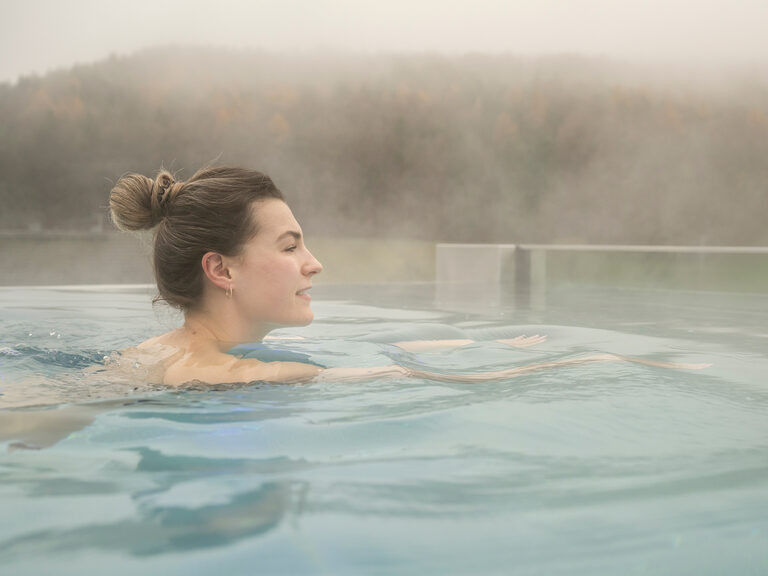 Eine Frau blickt von der Infinity-Kante des dampfenden Skypools über den Oberpfälzer Wald