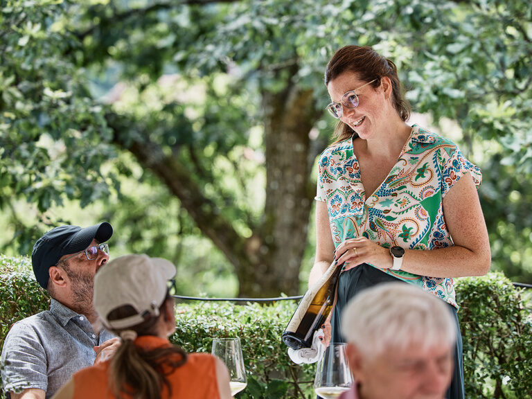 Eine Frau zeigt Gästen Rotwein.