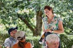 Eine Frau zeigt Gästen Rotwein.