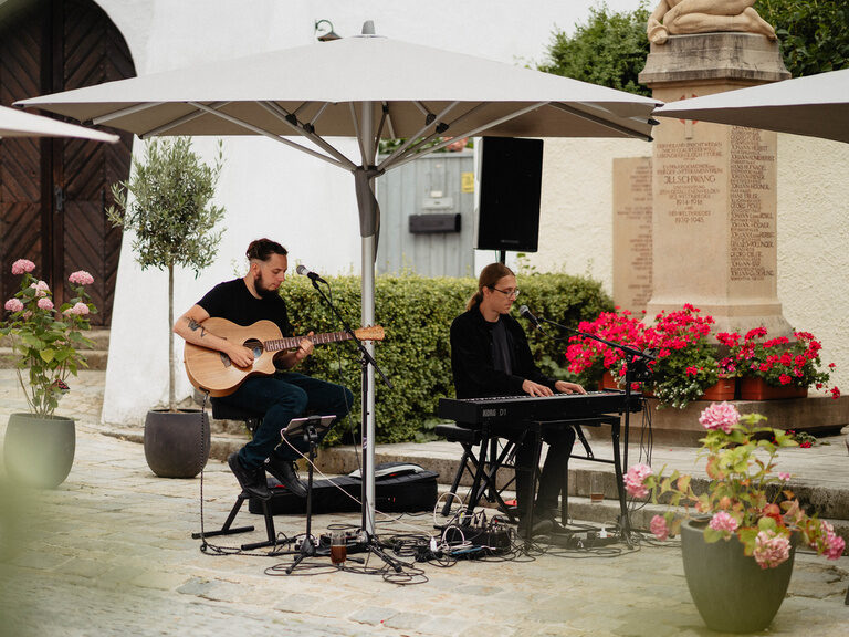Zwei Männer spielen unter einem Sonnenschirm auf Gitarre und Keyboard