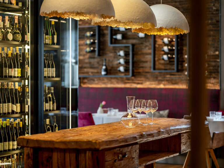 Ein großer Weinschrankt präsentiert die zahlreichen Weinflaschen im Weinkeller des Wellnesshotels und auf einem rustikalen Holztisch sind Weingläser aufgestellt