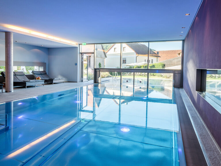Der große Innenpool des Wellnesshotels in der Oberpfalz ist direkt mit dem Aussenpool durch ein großes Fenster verbunden.