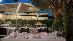 Die Terrasse ist für ein schickes Abendessen hergerichtet und mit Schirmen überdacht.