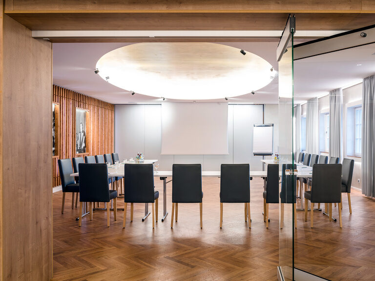 Ein großer Raum mit Glaswänden und einer Leinwand ist für eine Tagung bereit