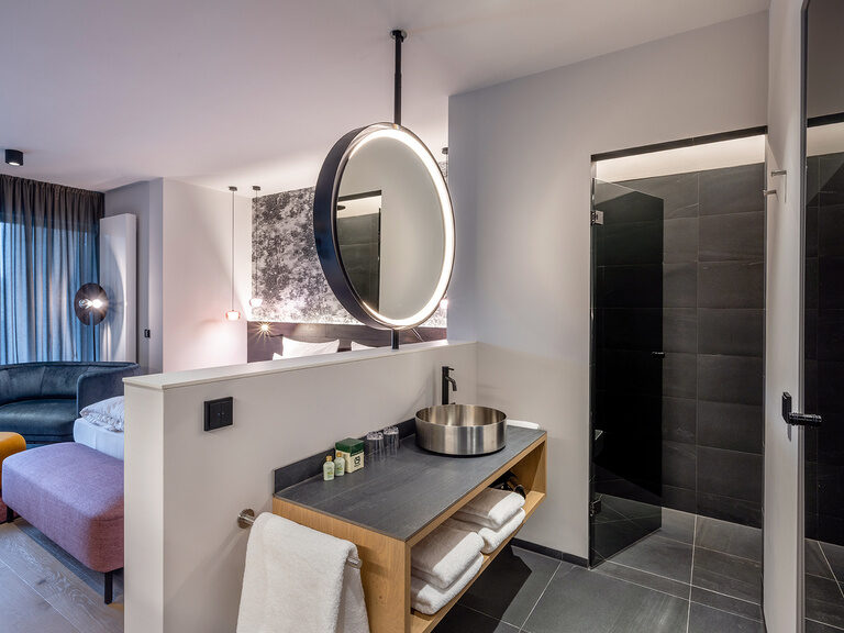 Der freihängende große runde Spiegel im offenen Badezimmer des Premium Deluxe Zimmers