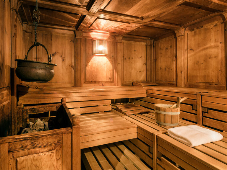 Die rustikale Stubensauna mit dunklem Holz und einem gusseisernen Topf