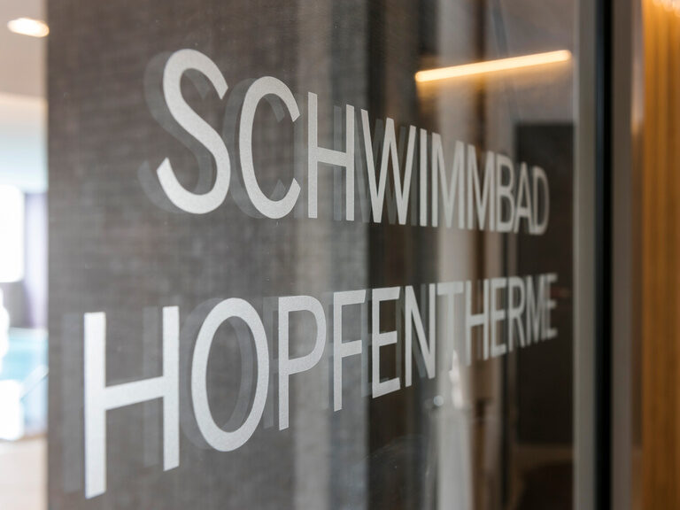 Auf eine Glastür ist in weißer Schrift Schwimmbad Hopfentherme geschrieben.