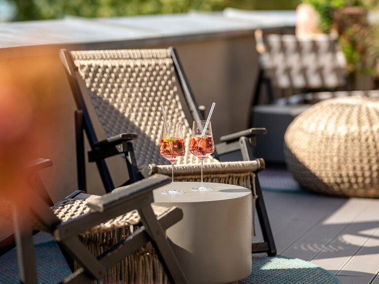 Ein Korbsessel auf der Poolterrasse mit bunten Blumen im Hintergrund.