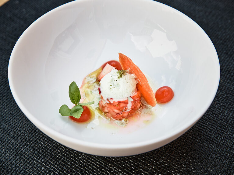 Ein Gericht, das mit Tomaten und grünen Blättern verziert ist, wartet darauf im Gourmetrestaurant Cheval Blance serviert zu werden