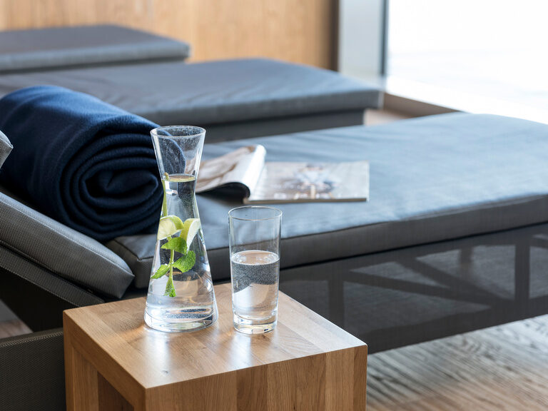 In dem Ruheraum des Wellnesshotels steht ein Wasserglas auf einem Tisch neben einer Liege.