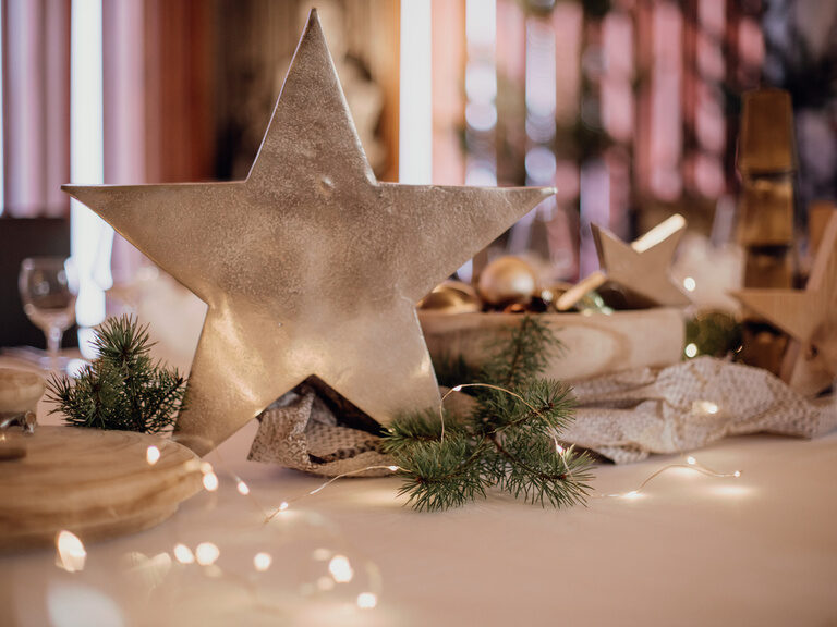 Ein Tisch ist mit Zweigen, einer Lichterkette und einem Stern im Mittelpunkt weihnachtlich dekoriert.