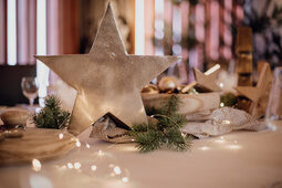 Ein Tisch ist mit Zweigen, einer Lichterkette und einem Stern im Mittelpunkt weihnachtlich dekoriert.