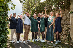 Eine Teil des Teams steht lachend und Weingläser hebend vor einer Mauer in der Oberpfalz