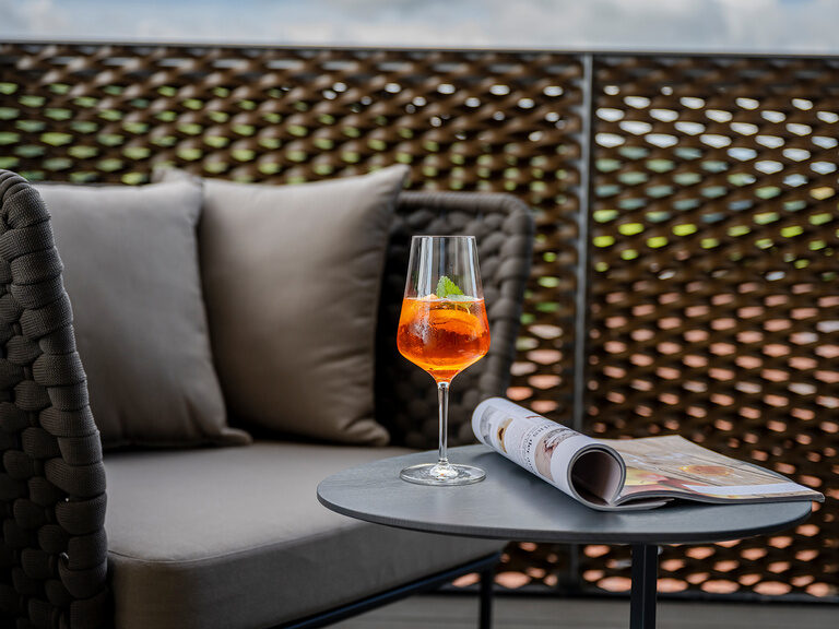 Ein Weinglas steht auf einem Tisch neben einer Couch auf der Terrasse.
