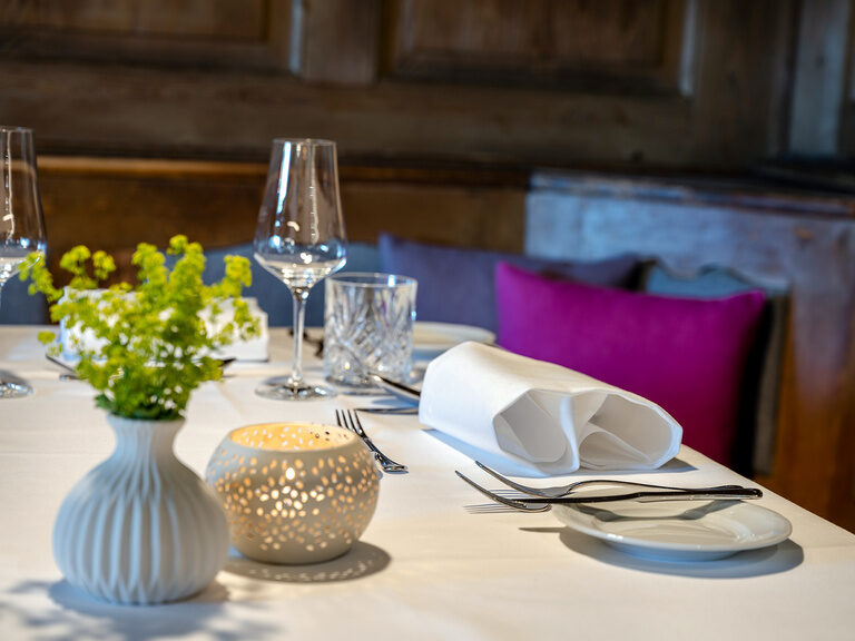 Ein Tisch in der Gaststube ist bereits für das Abendessen gedeckt und mit Blumen und Kerzen verziert.